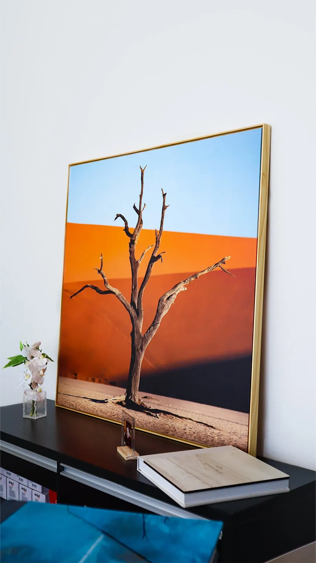 Árvore seca em exposição de arte com fundo de deserto laranja e céu azul, combinação de cores vibrantes e conceito de natureza.