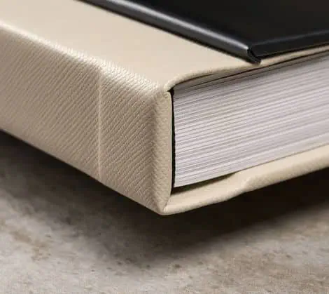 Livro grosso com capa de tecido bege e capa dura preta, sobre superfície de concreto.