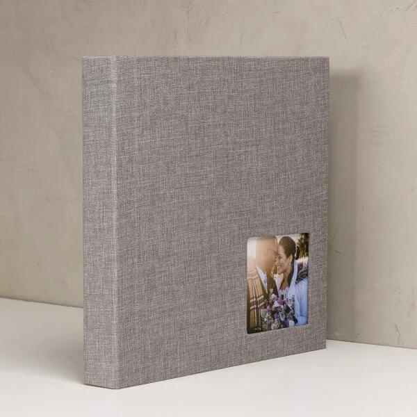 Álbum de fotos com capa de tecido cinza e janela com foto de casal apaixonado, ideal para recordações especiais.