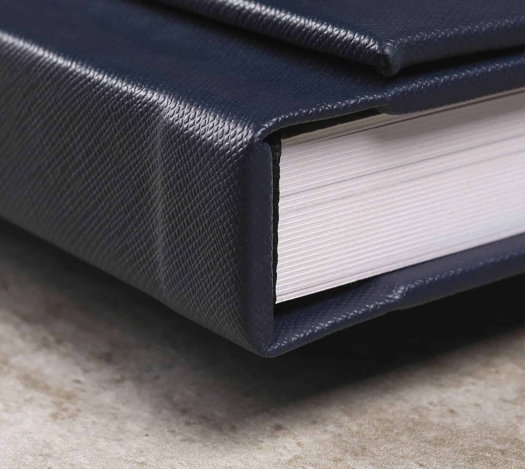 Capa de livro com acabamento em tecido sintético azul escuro e páginas brancas encadernadas duráveis.