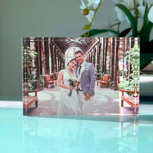 Porta Retrato em Acrílico Casal de casamento em estilo clássico em jardim com árbore e bancos de madeira.