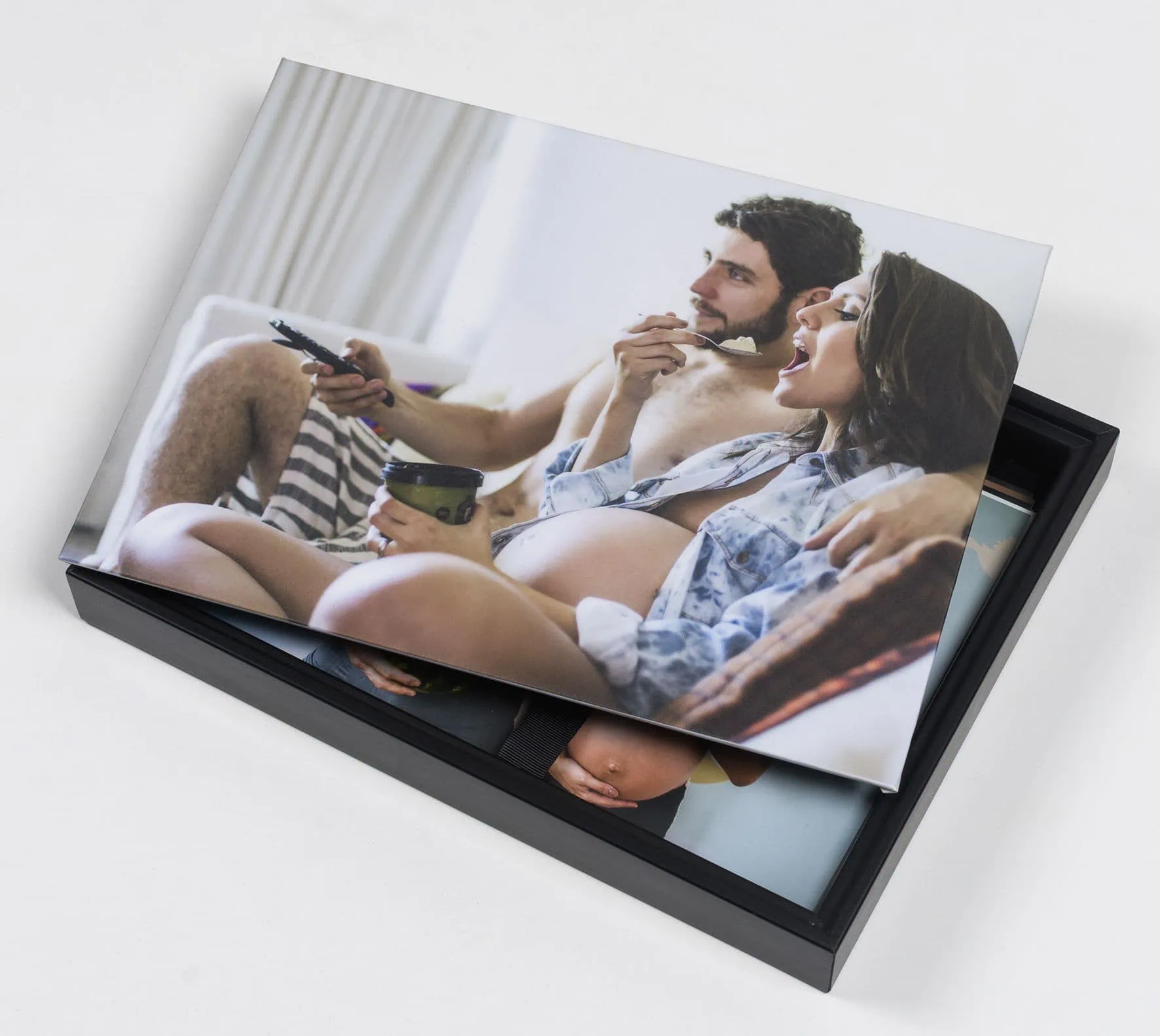 Casal grávida apreciando fotos impressas em álbum fotográfico personalizado.